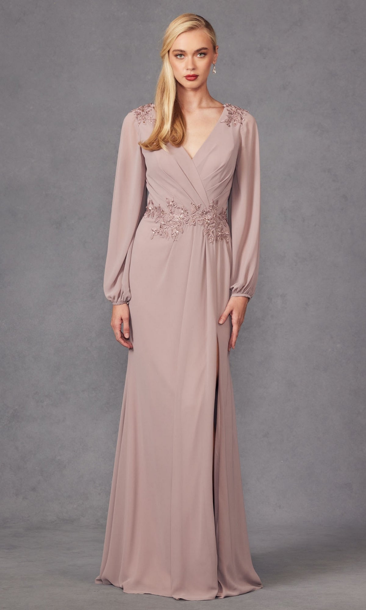 A woman wears the Juliet JTM16A V-Neck Long Sleeve Prom Gown in mauve with floral embroidery at the shoulders and waist, standing against a plain gray background.
